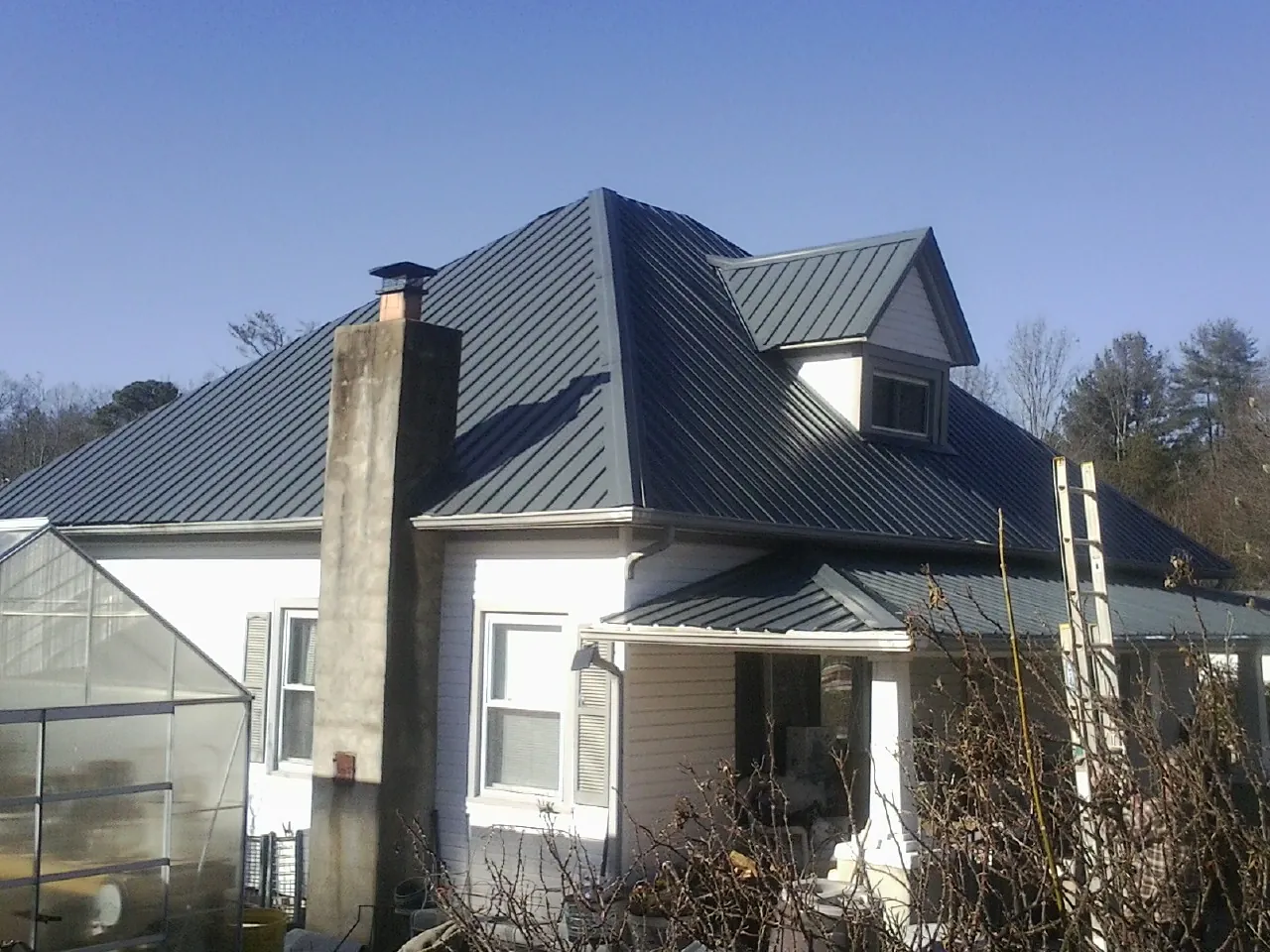 Dark blue standing seam metal roof on a white farmhouse with dormer — Slate & Tile Roof Repair by Roofing Brothers in Oakhurst