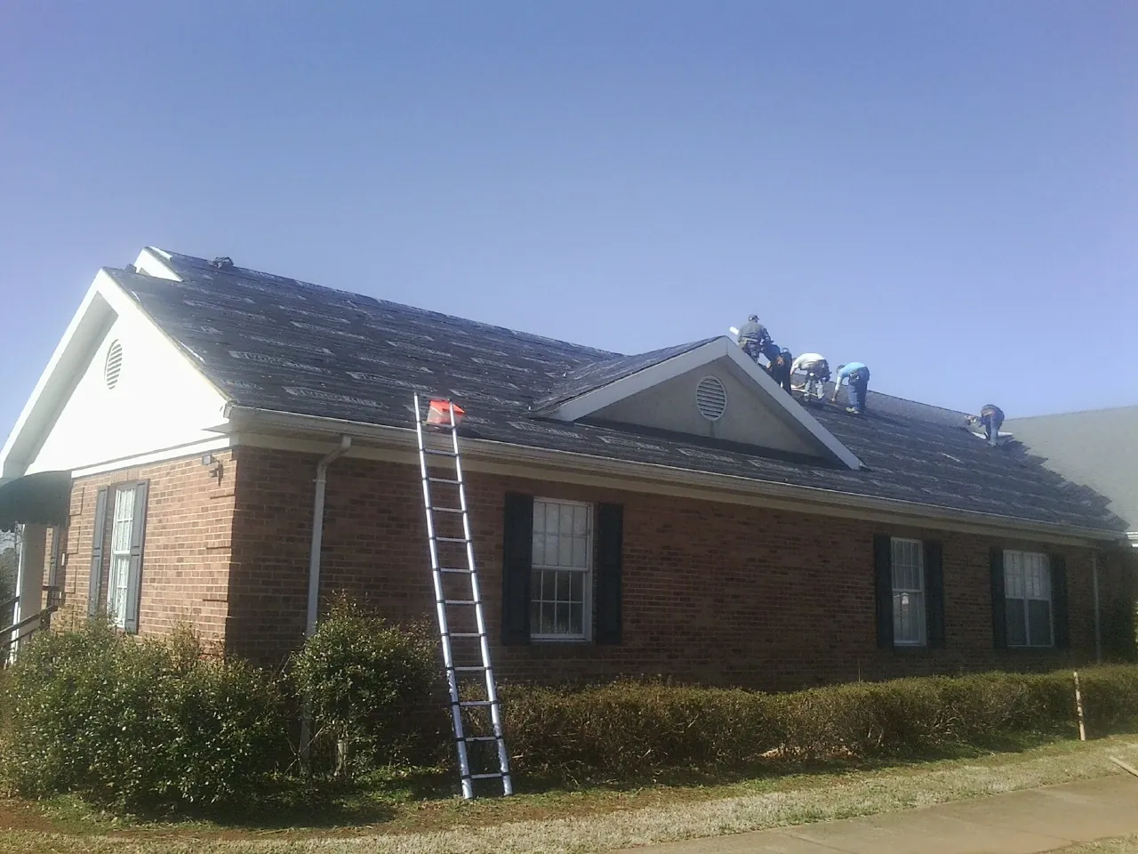 Crew tearing shingles off a brick ranch roof with a ladder set — Emergency Roof Repair work by our crew in Oakhurst
